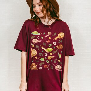 May include: A maroon t-shirt with a pattern of snails, leaves, and flowers. The text "karokumo" is printed on the bottom of the shirt.