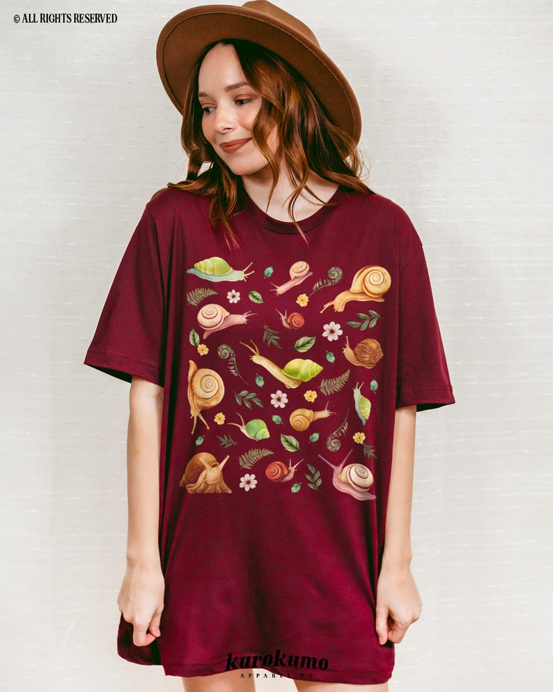 May include: A maroon t-shirt with a pattern of snails, leaves, and flowers. The text "karokumo" is printed on the bottom of the shirt.