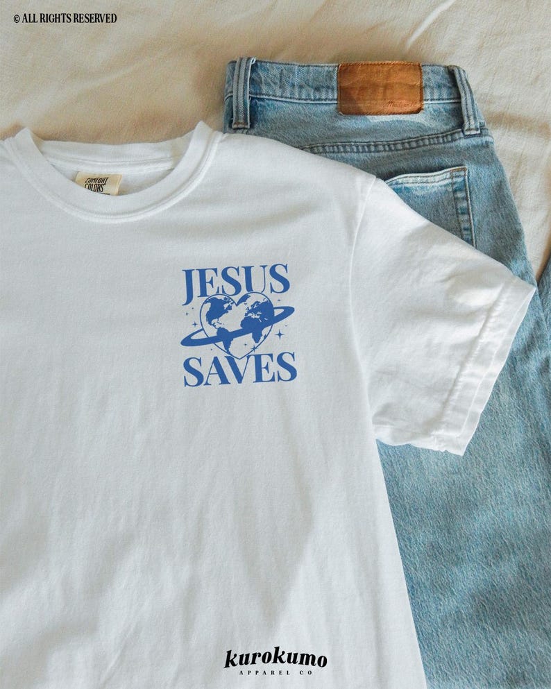 K&ouml;nnte beinhalten: Wei&szlig;es T-Shirt mit einem blauen Grafikdesign, das eine herzf&ouml;rmige Erde mit einem Ring darum und den Text "JESUS SAVES" zeigt. Das Shirt tr&auml;gt auch den Text "kurokumo APPAREL CO" unten.