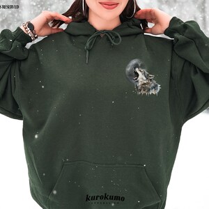 May include: A dark green hooded sweatshirt with a wolf howling at the moon graphic on the front. The graphic is in shades of gray and white.