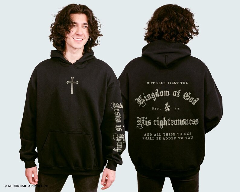 Op de afbeelding: Zwart hoodie met een kruis op de voorkant en de tekst "Jesus is King" op de linkermouw. De achterkant van de hoodie heeft de tekst "But seek first the Kingdom of God & His righteousness and all these things shall be added to you" in een decoratief lettertype.