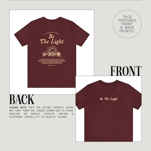 May include: Burgundy t-shirt with a graphic print of a mountain range and the text "In this dark world, Be the light." on the back and the text "Be the light" on the front.