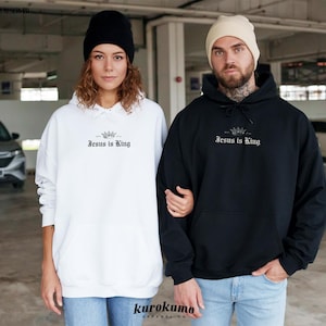 May include: Two people wearing hoodies with the text "Jesus is King" printed on the front. The person on the left is wearing a white hoodie and the person on the right is wearing a black hoodie.