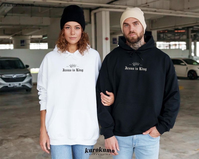 May include: Two people wearing hoodies with the text "Jesus is King" printed on the front. The person on the left is wearing a white hoodie and the person on the right is wearing a black hoodie.