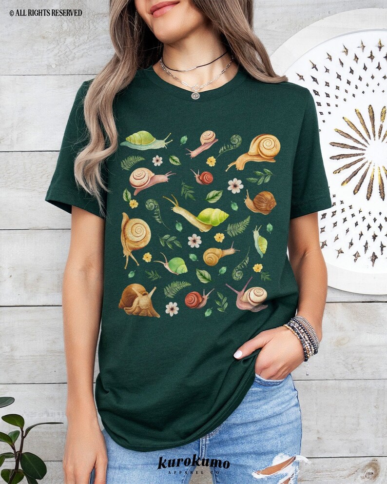 May include: A dark green t-shirt with a pattern of snails and leaves. The snails are brown and yellow with white shells. The leaves are green and there are small white flowers scattered throughout the pattern.