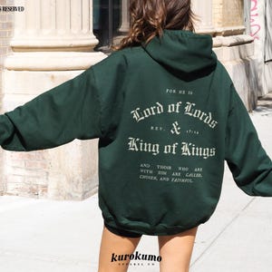 May include: A dark green hooded sweatshirt with the text "FOR HE IS Lord of Lords REV. & King of Kings AND THOSE WHO ARE WITH HIM ARE CALLED, CHOSEN, AND FAITHFUL" printed on the back.