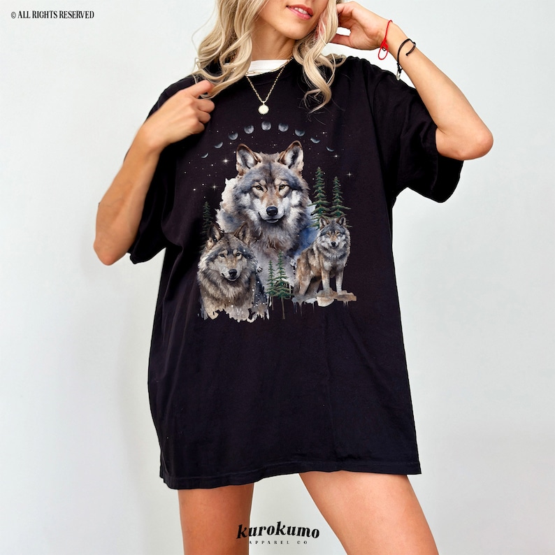 May include: Black t-shirt with a graphic print of three wolves in a forest setting with a crescent moon and stars. The text "kurokumo apparel co." is printed on the bottom of the shirt.