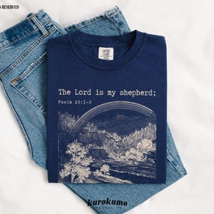 Puede incluir: Una camiseta azul marino con un gr&aacute;fico blanco de un paisaje y el texto "The Lord is my shepherd; Psalm 23:1-3".