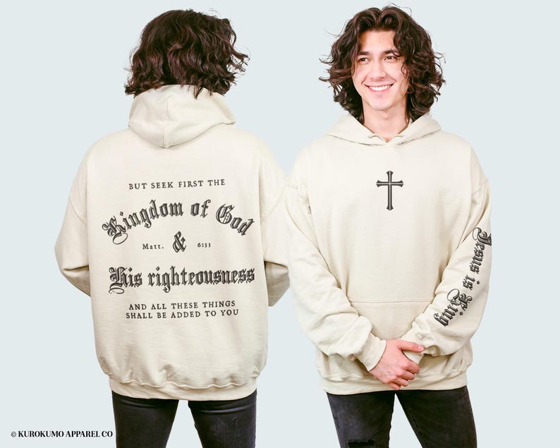 Op de afbeelding: Een beige hoodie met een zwarte print die "But seek first the Kingdom of God Matt. & 6:33 His righteousness And all these things shall be added to you" zegt. De rechtermouw heeft een zwarte print die "Jesus is King" zegt.