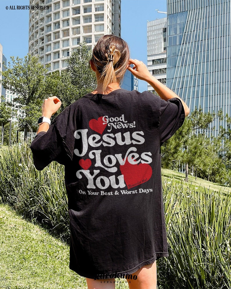 May include: Black t-shirt with a white graphic that says "Good News! Jesus Loves You" with red hearts. The text below the graphic says "On Your Best & Worst Days".
