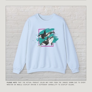 Puede incluir: Sudadera azul claro con un gr&aacute;fico de dos orcas nadando en un dise&ntilde;o abstracto turquesa y verde azulado. El dise&ntilde;o est&aacute; enmarcado en un rect&aacute;ngulo negro y rosa.