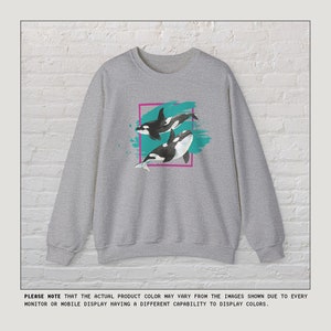 Puede incluir: Sudadera gris con un estampado gr&aacute;fico de dos orcas nadando en agua turquesa. Las orcas son negras y blancas con un contorno rosa alrededor del gr&aacute;fico.