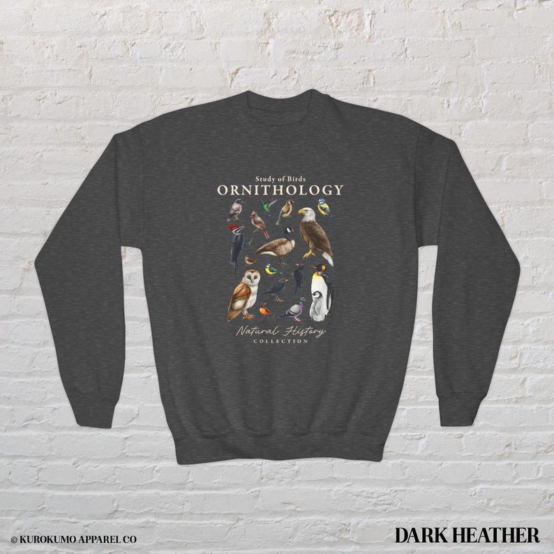 May include: Dark heather gray sweatshirt featuring a detailed illustration of various birds. The design includes an owl, eagle, and penguin, with the text "Study of Birds ORNITHOLOGY Natural History Collection."