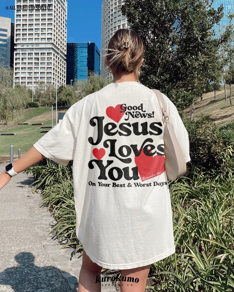 May include: White t-shirt with a graphic print of a red heart and the text "Good News! Jesus Loves You. Remember that on your best and worst days."