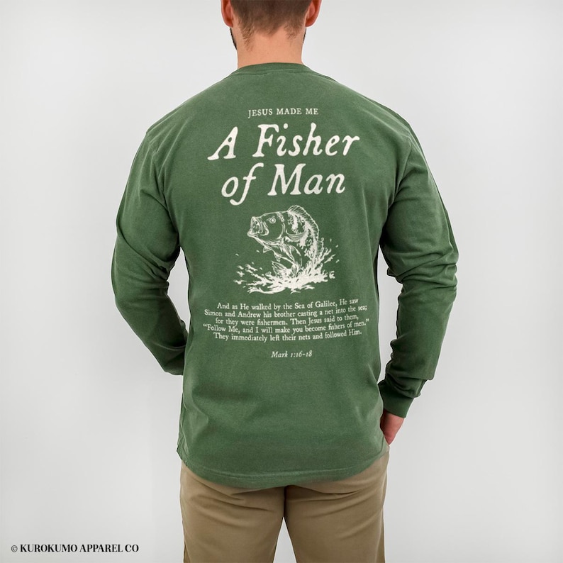 May include: Green long-sleeve shirt with white text and a fish graphic. The text reads "JESUS MADE ME A Fisher of Man" with a Bible verse below. The shirt is a solid colour and has long sleeves.