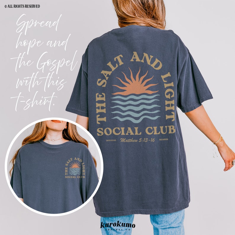 May include: A navy blue t-shirt with a graphic of a sunset over water and the text "The Salt and Light Social Club" with the Bible verse Matthew 5:13-16.