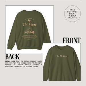 May include: A green sweatshirt with a front and back print. The front print says "Be The Light" and the back print says "In this dark world, Be The Light" with a mountain range and sun graphic.
