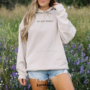 Pu&ograve; includere: Una felpa con cappuccio beige con cappuccio con coulisse e tasca a marsupio. La felpa ha la scritta "Do Not Worry" stampata sul davanti in nero.