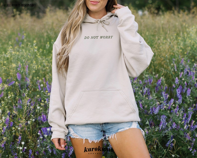 Pu&ograve; includere: Una felpa con cappuccio beige con cappuccio con coulisse e tasca a marsupio. La felpa ha la scritta "Do Not Worry" stampata sul davanti in nero.