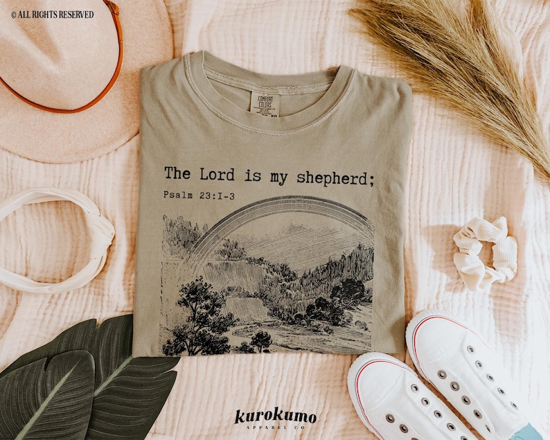 Puede incluir: Una camiseta verde claro con el texto "The Lord is my shepherd; Psalm 23:1-3" impreso en la parte delantera. La camiseta presenta una ilustraci&oacute;n en blanco y negro de un arco&iacute;ris y un paisaje.