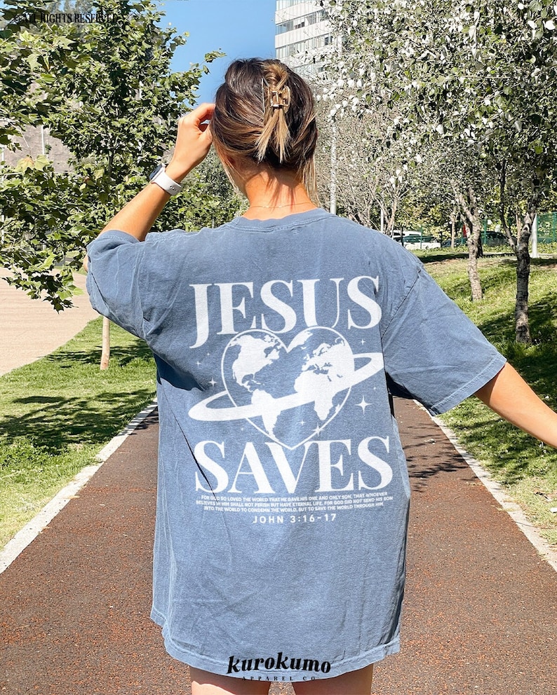 K&ouml;nnte beinhalten: Ein blaues T-Shirt mit einer wei&szlig;en Grafik der Welt in einem Herzen mit einem Ring darum. Der Text "JESUS SAVES" ist &uuml;ber der Grafik gedruckt. Der Text "FOR GOD SO LOVED THE WORLD THAT HE GAVE HIS ONLY BEGOTTEN SON, THAT WHOSOEVER BELIEVETH IN HIM SHOULD NOT PERISH BUT HAVE EVERLASTING LIFE. FOR GOD SENT NOT HIS SON INTO THE WORLD TO CONDEMN THE WORLD; BUT THAT THE WORLD THROUGH HIM MIGHT BE SAVED. JOHN 3:16-17" ist unter der Grafik gedruckt.