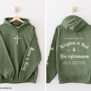 Op de afbeelding: Een groene hoodie met de tekst "Jesus is King" op de ene mouw en "But seek first the Kingdom of God & His righteousness And all these things shall be added to you" op de andere mouw.