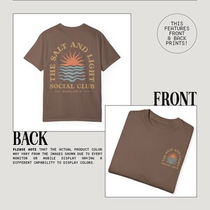 May include: A brown t-shirt with a graphic print on the back that says "The Salt and Light Social Club" with a sun and waves design. The front of the shirt has a smaller version of the same graphic print.