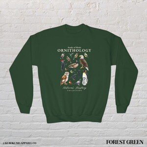 May include: Forest green sweatshirt featuring a detailed illustration of various bird species. The design includes the text "Study of Birds ORNITHOLOGY Natural History Collection". The sweatshirt is a comfortable, long-sleeved garment.