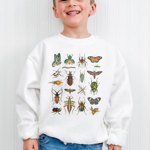 May include: White sweatshirt with a colorful insect and butterfly graphic print. The print features a variety of insects, including beetles, butterflies, and moths.