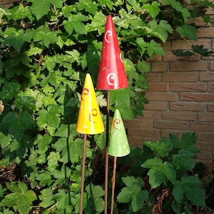 Könnte beinhalten: Drei Keramik-Gartenstecker in Form von Kegeln. Der höchste Kegel ist rot mit weißen Wirbeln, der mittlere Kegel ist gelb mit weißen Wirbeln und der kleinste Kegel ist grün mit weißen Wirbeln.