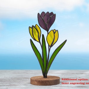 May include: A stained glass bouquet of three tulips, one purple and two yellow, on a wooden stand. Additional option: laser engraving on a stand.