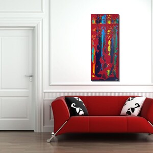 Könnte beinhalten: Abstraktes Gemälde mit leuchtenden Farben, darunter Rot, Blau, Gelb und Grün, auf einer weißen Leinwand. Das Gemälde wird an einer weißen Wand in einem Raum mit einem roten Sofa und weißen Kissen ausgestellt.