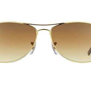 Puede incluir: Gafas de sol aviador doradas con lentes de degradado marr&oacute;n. Las gafas tienen el logotipo de Ray-Ban en la lente izquierda.