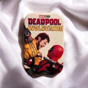 Könnte beinhalten: Eine rechteckige Metalldose mit dem Filmplakat von Marvel Studios Deadpool & Wolverine. Die Grafik zeigt Wolverine im gelben Anzug mit ausgefahrenen Krallen gegenüber Deadpool in roter Maske und Anzug, mit dem Titeltext darüber.