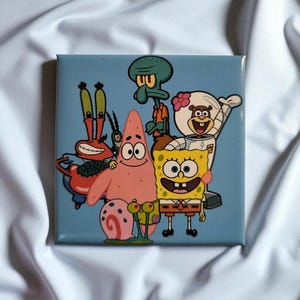 Könnte beinhalten: Eine quadratische Keramikfliese mit einer farbenfrohen Illustration von SpongeBob Schwammkopf, Patrick Star, Thaddäus Tentakel, Mr. Krabs, Sandy Cheeks, Gary der Schnecke und Plankton vor einem hellblauen Hintergrund mit glänzender Oberfläche.
