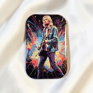 Könnte beinhalten: Rechteckiger Magnet mit einer farbenfrohen Illustration eines Gitarre spielenden Musikers. Das Bild hat einen lebendigen, abstrakten Hintergrund mit Farbspritzern in Blau, Lila, Gelb und Rot. Der Musiker trägt eine Jeansjacke und eine dunkle Hose.