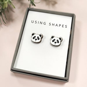 May include: A pair of wooden panda bear stud earrings in a small white box with the text "USING SHAPES" printed on the front.
