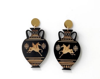 May include: A pair of black and gold earrings shaped like ancient Greek urns with a winged horse design. The earrings have gold accents and are made of wood.