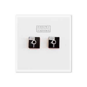 Könnte beinhalten: Ein Paar schwarze Ohrringe in Form von alten Disketten. Die Ohrringe werden von der Firma "USINGSHAPES" hergestellt.