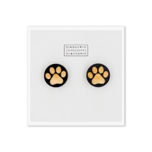 May include: A pair of wooden earrings with a paw print design. The earrings are black with a light brown paw print.