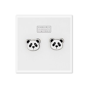 May include: A pair of white wooden panda bear earrings with black eyes, nose, and ears. The earrings are packaged on a white card with the text "USING SHAPES" printed in black.