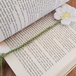 May include: A green crocheted bookmark with a white crocheted daisy flower on top. The bookmark has a tassel at the bottom.