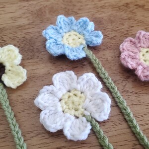 May include: Four crocheted flowers with green stems. The flowers are yellow, blue, white, and pink.