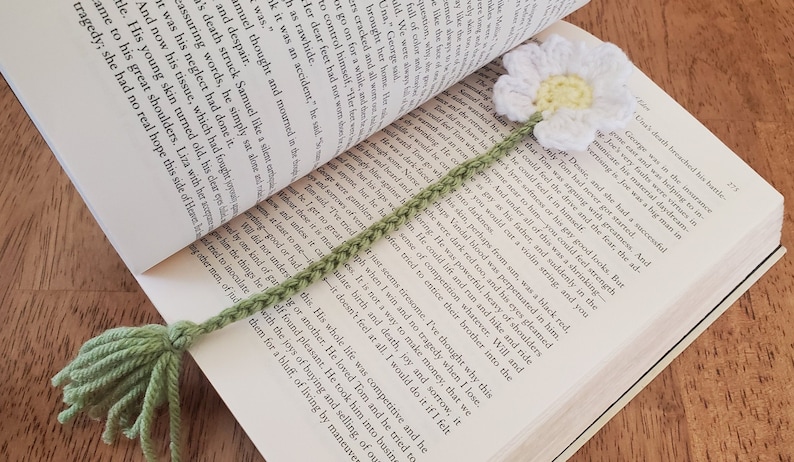 May include: A green crocheted bookmark with a white crocheted daisy flower on top. The bookmark has a tassel at the bottom.