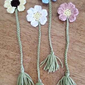 May include: Four crocheted flower bookmarks with green tassels. The flowers are yellow, white, light blue, and pink.