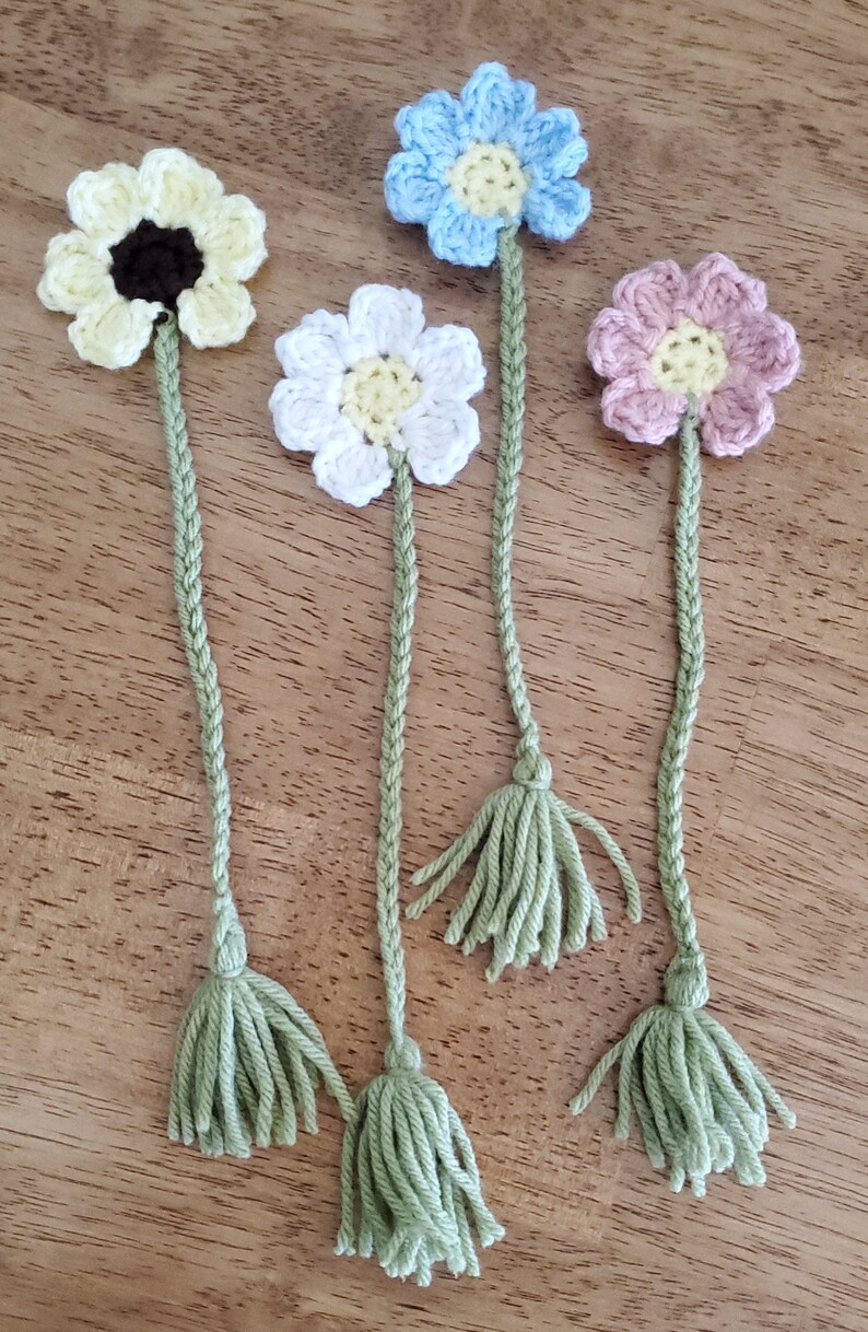 May include: Four crocheted flower bookmarks with green tassels. The flowers are yellow, white, light blue, and pink.