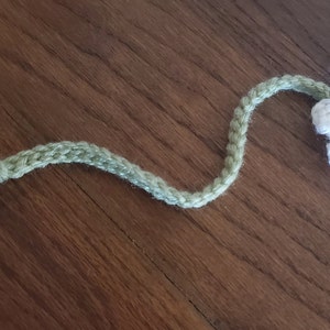 May include: A crocheted bookmark shaped like a daisy with a green stem and tassel. The flower is white with a yellow centre.