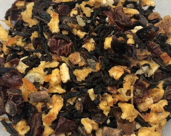 May include: A close-up of a blend of black tea leaves, orange peel, and dried cranberries. The tea is a mix of dark brown, orange, and red pieces.