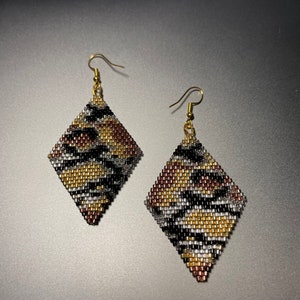 May include: A pair of gold dangle earrings with a diamond-shaped design. The earrings are made of small beads in a black, brown, gold, and silver pattern.