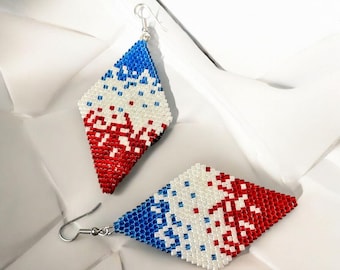 May include: A pair of diamond-shaped earrings with a patriotic color scheme. The earrings are beaded with red, white, and blue beads. The top portion is blue, transitioning to white, and then red at the bottom. The earrings have silver-colored hooks.